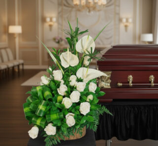 Arreglo de flores blancas con rosas y anturios sobre base de madera al lado de un ataúd de madera barnizada en una elegante sala de velación