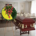 Corona fúnebre redonda con flores amarillas y rojas sobre caballete junto a ataúd de madera barnizada en una sala velatoria