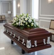 Ataúd de madera oscura con herrajes plateados y arreglo de flores blancas en una sala de velatorio elegante