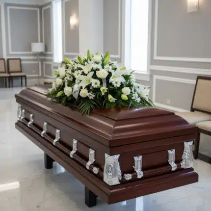 Ataúd de madera oscura con herrajes plateados y arreglo de flores blancas en una sala de velatorio elegante