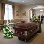 Ataúd de madera oscura con arreglos florales blancos en una sala de velatorio elegante