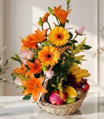 Arreglo Basilio, cesta frutal con rosas, lirios naranjas, gerberas amarillas, uvas, plátanos, manzanas, kiwi y pitahaya sobre