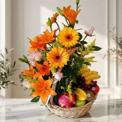 Arreglo Basilio, cesta frutal con rosas, lirios naranjas, gerberas amarillas, uvas, plátanos, manzanas, kiwi y pitahaya sobre