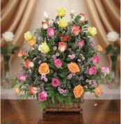 Arreglo floral DONNIA en cesta de mimbre con 34 rosas de colores variados (rosas, amarillas, naranjas) y follaje verde, sobre