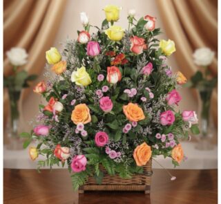 Arreglo floral DONNIA en cesta de mimbre con 34 rosas de colores variados (rosas, amarillas, naranjas) y follaje verde, sobre