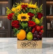 Arreglo floral Adriano con rosas rojas, girasoles vibrantes, naranjas, peras, uvas y fresas en una caja de madera sobre mármo