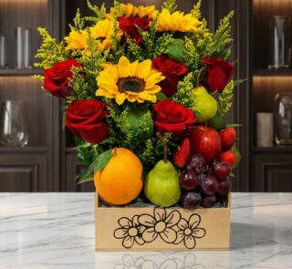 Arreglo floral Adriano con rosas rojas, girasoles vibrantes, naranjas, peras, uvas y fresas en una caja de madera sobre mármo