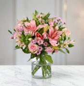 Arreglo floral ANNA con rosas y lirios rosados, alstroemerias y margaritas, en un jarrón de cristal sobre una mesa de mármol