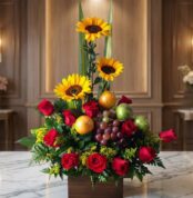 Arreglo floral Batista con rosas rojas, girasoles vibrantes, uvas, naranjas y manzanas verdes, sobre una mesa de mármol en un