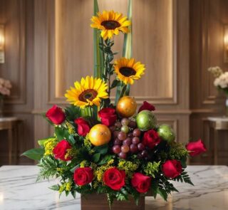 Arreglo floral Batista con rosas rojas, girasoles vibrantes, uvas, naranjas y manzanas verdes, sobre una mesa de mármol en un