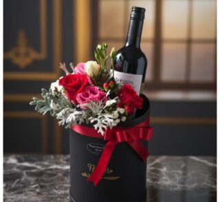 Arreglo floral BENTO con rosas rojas y rosadas, follaje verde y una botella de vino tinto en una caja negra con lazo rojo, so