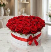 Arreglo floral CAMILA con 24 rosas rojas premium en una elegante caja blanca en forma de corazón, adornada con un lazo rojo,