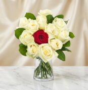 Arreglo floral CARLA con 12 rosas de tallo largo, una roja central y once blancas, en un jarrón de cristal sobre mármol.