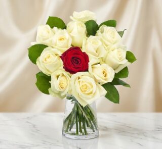 Arreglo floral CARLA con 12 rosas de tallo largo, una roja central y once blancas, en un jarrón de cristal sobre mármol.
