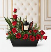 Arreglo floral CINZIA con 12 rosas rojas frescas, follaje verde variado y una botella de vino tinto, presentado en una base n