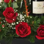 Primer plano extremo de arreglo floral CINZIA con 12 rosas rojas, gotas de rocío, follaje verde y botella de vino tinto.