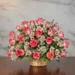 Arreglo floral Emilia con 32 rosas blush frescas, alstroemerias blancas y follaje verde en una canasta de mimbre sobre una me