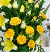 Primer plano extremo de un arreglo floral exótico Amaretto con rosas amarillas, lirios blancos y gerberas amarillas, mostrand