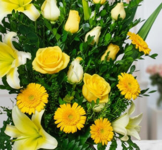 Primer plano extremo de un arreglo floral exótico Amaretto con rosas amarillas, lirios blancos y gerberas amarillas, mostrand