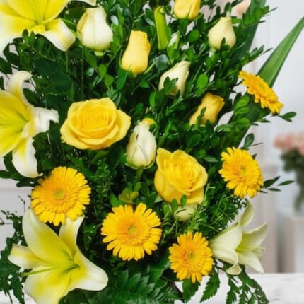 Primer plano extremo de un arreglo floral exótico Amaretto con rosas amarillas, lirios blancos y gerberas amarillas, mostrand