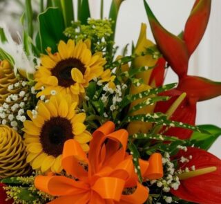 Primer plano extremo de Arreglo Floral Exótico Antídoto con girasoles, heliconias rojas, flores de jengibre y lazo naranja, c