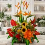 Arreglo floral exótico Antídoto con aves del paraíso, anturios rojos, girasoles y piñas decorativas sobre mármol.