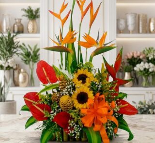 Arreglo floral exótico Antídoto con aves del paraíso, anturios rojos, girasoles y piñas decorativas sobre mármol.