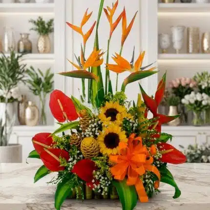 Arreglo floral exótico Antídoto con aves del paraíso, anturios rojos, girasoles y piñas decorativas sobre mármol.