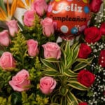Primer plano extremo de un arreglo floral exótico con rosas rosadas y rojas, follaje verde y un globo rojo de 'Feliz Cumpleañ