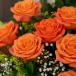Primer plano extremo de un arreglo floral con rosas naranjas vibrantes, gotas de rocío sutiles y follaje verde, destacando la