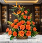 Impresionante arreglo floral exótico con vibrantes rosas naranjas y aves del paraíso, presentado en una cesta de mimbre sobre