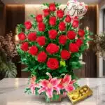Arreglo Floral Exótico Gamma con rosas rojas abiertas, lirios rosados, follaje verde y chocolates Ferrero Rocher sobre mármol