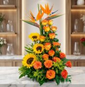 Arreglo floral exótico Intocable con aves del paraíso, rosas naranjas y girasoles, sobre mármol en floristería premium.
