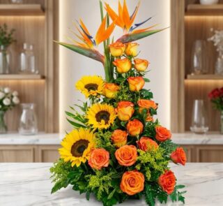 Arreglo floral exótico Intocable con aves del paraíso, rosas naranjas y girasoles, sobre mármol en floristería premium.