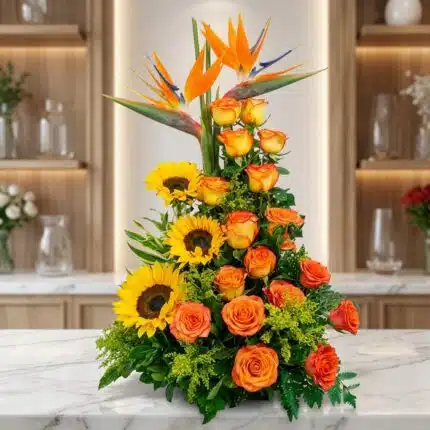 Arreglo floral exótico Intocable con aves del paraíso, rosas naranjas y girasoles, sobre mármol en floristería premium.