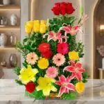 Arreglo floral exótico Paraíso con lirios rosados, rosas rojas y amarillas, y gerberas de varios colores, sobre una superfici