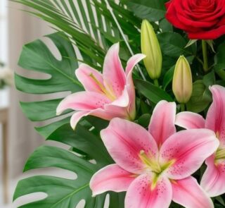 Primer plano extremo de un arreglo floral exótico con lirios rosas vibrantes, capullos de lirio, una rosa roja y hojas de mon