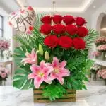 Arreglo floral exótico primaveral con rosas rojas vibrantes, lirios rosados abiertos y follaje exuberante, sobre mármol en fl