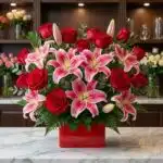 Arreglo floral exótico Feliz Contigo con rosas rojas abiertas y lirios rosados vibrantes, sobre mármol blanco en floristería