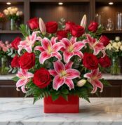 Arreglo floral exótico Feliz Contigo con rosas rojas abiertas y lirios rosados vibrantes, sobre mármol blanco en floristería