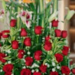 Primer plano extremo de un arreglo floral exótico Tucana con rosas rojas vibrantes, lirios y follaje verde, destacando textur