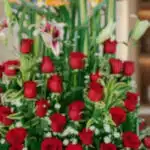 Primer plano extremo de un arreglo floral exótico Tucana con rosas rojas vibrantes, lirios y follaje verde, destacando textur