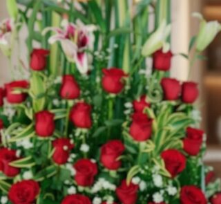 Primer plano extremo de un arreglo floral exótico Tucana con rosas rojas vibrantes, lirios y follaje verde, destacando textur