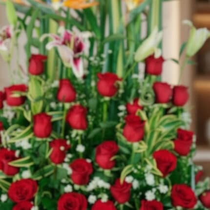 Primer plano extremo de un arreglo floral exótico Tucana con rosas rojas vibrantes, lirios y follaje verde, destacando textur