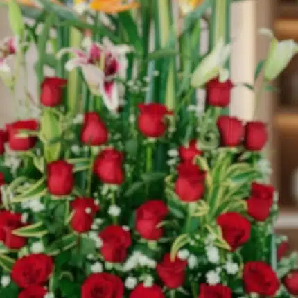 Primer plano extremo de un arreglo floral exótico Tucana con rosas rojas vibrantes, lirios y follaje verde, destacando textur