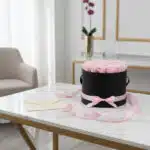 Arreglo Floral Francesca con 21 rosas rosadas en un cilindro negro, sobre mesa de mármol con tarjeta de regalo y cinta rosa.