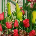 Primer plano extremo de Arreglo Floral con Frutas Akebia, mostrando rosas rojas vibrantes, uvas frescas y follaje verde con g