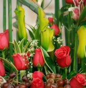 Primer plano extremo de Arreglo Floral con Frutas Akebia, mostrando rosas rojas vibrantes, uvas frescas y follaje verde con g