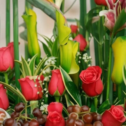 Primer plano extremo de Arreglo Floral con Frutas Akebia, mostrando rosas rojas vibrantes, uvas frescas y follaje verde con g