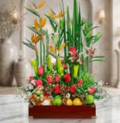 Arreglo floral Akebia con aves del paraíso, rosas rojas, lirios, orquídeas y frutas frescas sobre mármol, fondo de floristerí